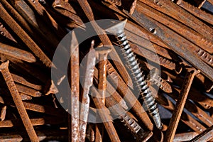 rusty iron nails piled up in disarray and a new chrome screw on top