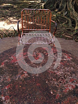 Rusty iron table and chairs with tree roots in the background.