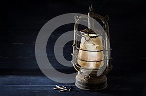 Rusty kerosene lantern shines undaunted with light in the dark, obsolete technology in times of modern energy-saving lamps,
