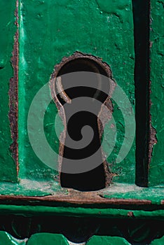 A rusty keyhole in an old cracky green metal door