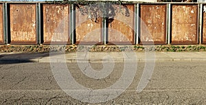 Rusty metal boards with scraped street billboards and ivy on top, at the roadside. Concrete sidewalk and street in front