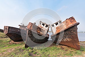 Rusty metal hulls of river vessels stand on the banks of the Barguzin River near the Barguzinsky Bay of Baikal.