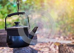 rusty metal kettle on burning firewood pile with blur background in camp