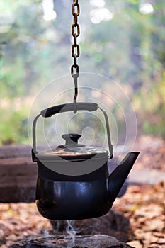 rusty metal kettle on burning firewood pile with blur background in camp