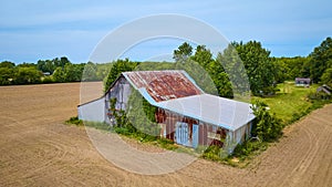 Rusty metal roof on barn with green vines growing on side in middle of nowhere aerial