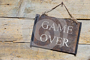 Rusty metal sign on wooden table, text game over