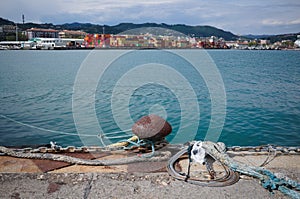 Rusty mooring bollard with ropes and chain on pier in port of La Spezia, Italy