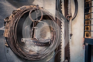 Rusty old bear trap hanging on wall in hunterÂ´s shed with wire coil and bone saws