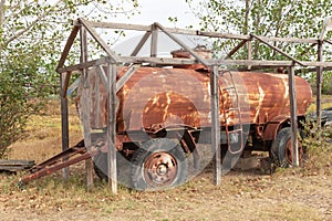 Rusty old big barrel on wheels.Broken tank for liquids,standing under a wooden structure.Ð¡oncept of abandoned unnecessary