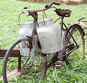 Rusty old bike of the milkman with two old milk cans and broken