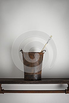 Rusty old bucket on a wooden shelf with a single artist brush