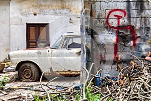 Rusty old car parked next to a brick wall with communism sign (hammer and sickle) on it