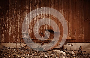 A rusty old horse plow in front of a weathered wooden barn wall in brown color tone for a western look