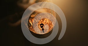 A rusty old large vintage lock hangs on a chain, closing the old door, in the semi-darkness, illuminated by a beam of light