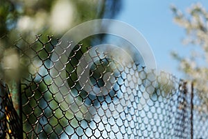 Rusty old mesh cage in garden with green trees and blue sky as background. Steel iron metal fence with wire mesh at