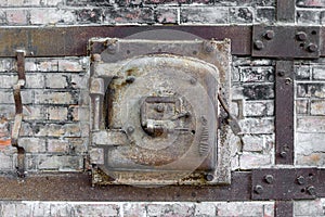 Rusty old metal hatch door of a red brick kiln.