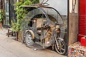A rusty and old motorized rickshaw in a back alley in a Beijing