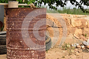 A rusty old oil can stands in arid, hot land next to old car tires on dry earth