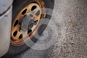 Rusty old truck wheel parked in random area. Oxidized black colored ream set tire. Not so good condition parts of the vehicle. It