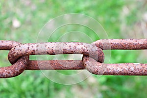 Rusty oxidized brown link of an old strong forged metal iron chain against a background of green