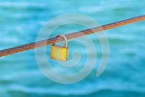 Rusty Padlock hanging on a iron wire on the sea water background.