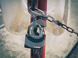 Rusty padlock hangs on a red pipe with a chain