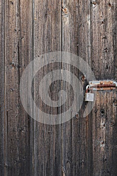 A rusty padlocked bolt on weathered wooden gate