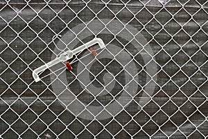 Rusty plastic garment hanger hanging on chain link fence with a gray tarp behind the fence