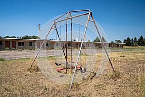 Rusty playground equipment with a swingset sits in a courtyard of an abandoned motel