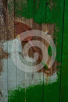 Rusty red handle of door on old wood door with remnants of green paint. Vertical wood texture with