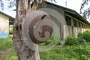 Rusty School Bell For Signalize about a School Brake Hanging on the Tree Near African school building in Primary School