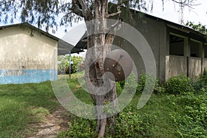 Rusty School Bell For Signalize about a School Brake Hanging on the Tree Near African school building in Primary School