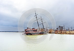 Rusty shipwreck marooned near shore on lake under a stormy blue