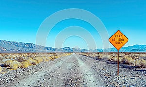 A rusty sign on a desolate desert road under a clear blue sky. Generate AI