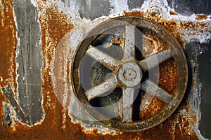Rusty six-pronged wheel set into an old rusty metal wall background