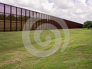 Rusty steel fence on the USA - Mexico border in Laredo, Texas, with grass lawn in front