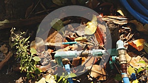 Rusty Water Valve and Pipe on Wet Garden Ground with Dry Leaves, Grass and Wood