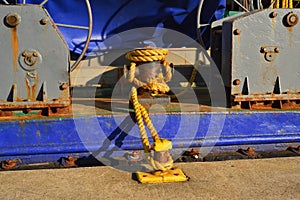 A rusty yellow mooring bitt, mooring line and dark blue bulwark of a dredger