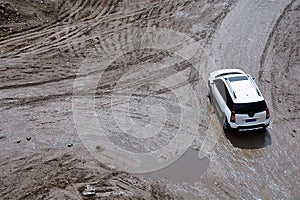 Rutting and white car on a dirt road.