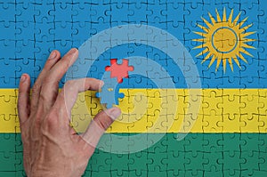 Rwanda flag is depicted on a puzzle, which the man`s hand completes to fold