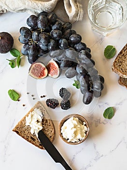 Rye bread and a knife with cream cheese and various fruits on a marble background. Cooking toast with cheese and berries.