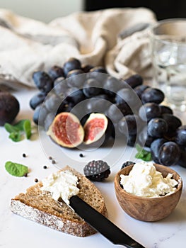 Rye bread and a knife with cream cheese and various fruits on a marble background. Cooking toast with cheese and berries.