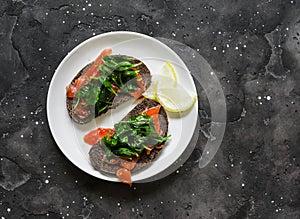 Rye bread sandwich with homemade salted salmon and passivated spinach on a dark background, top view. Delicious tapas