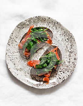 Rye bread sandwich with homemade salted salmon and passivated spinach on a light background, top view