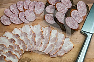 Rye bread sandwiches with smoked sausage and sliced bacon on wooden board.