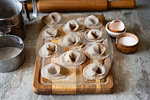 Rye dumplings with meat filling on a wooden board on a gray background. Preparation of dumplings from rye flour dough
