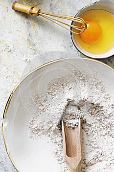 Rye flour with a wooden scoop next to a bowl of fresh egg flatlay