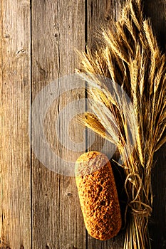 Rye spikelets and bread over wooden background