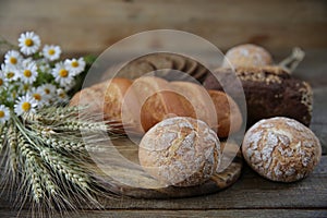 Rye and wheat fresh hot bread with ears and a bouquet of daisies on a wooden rustic background, close-up.
