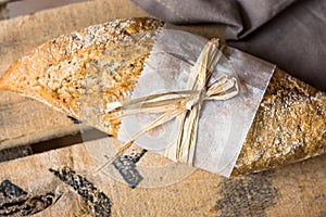 Rye whole wheat bread roll with golden crust wrapped in parchment paper on wood vintage box, grey linen napkin